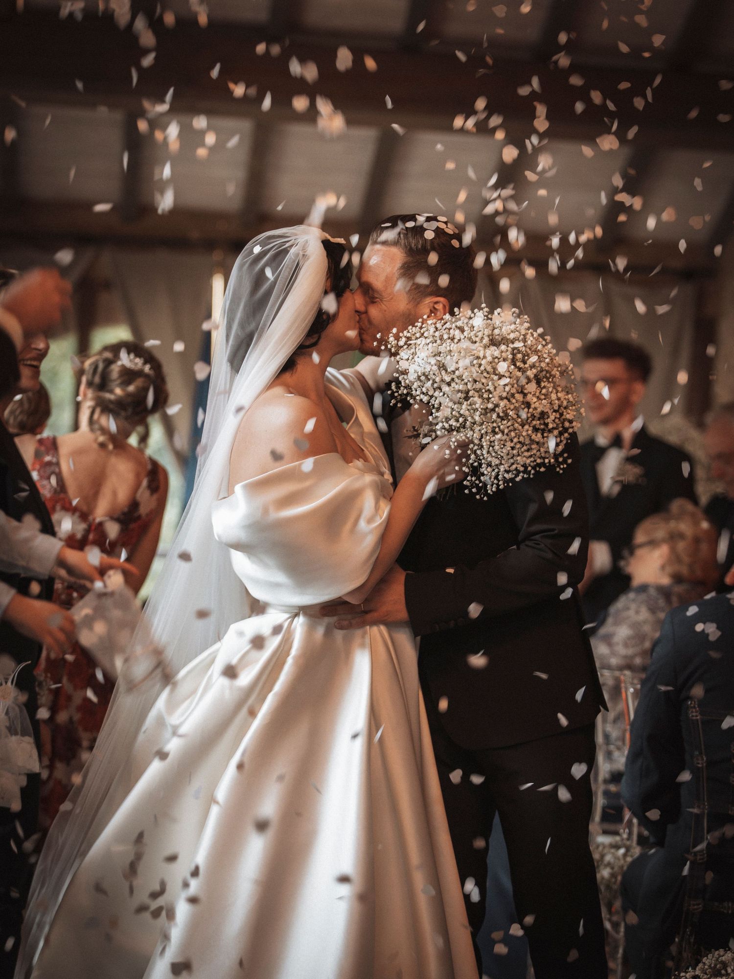 Wedding celebration with confetti falling around couple in elegant white dress and suit.