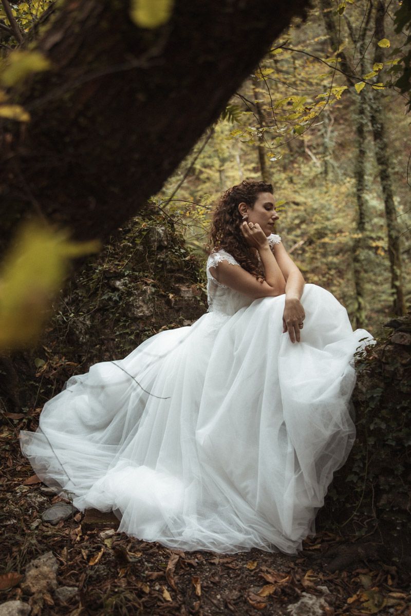 A flowing white wedding dress billows dramatically against an autumn forest backdrop.