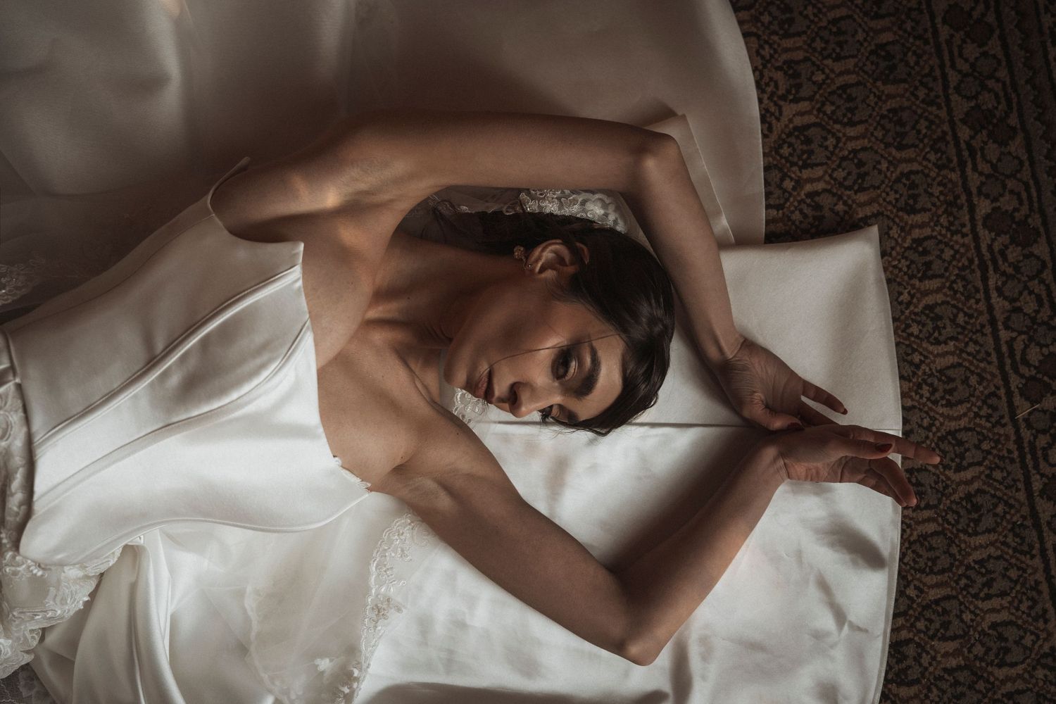 A person lies peacefully on white bedding while wrapped in soft fabric during a relaxing morning moment.
