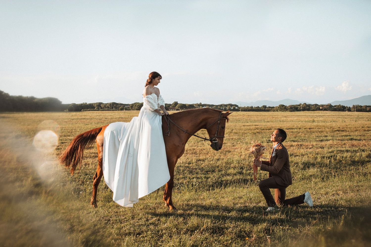 Panoramic view of couple in wedding attire walking through golden field at sunset.