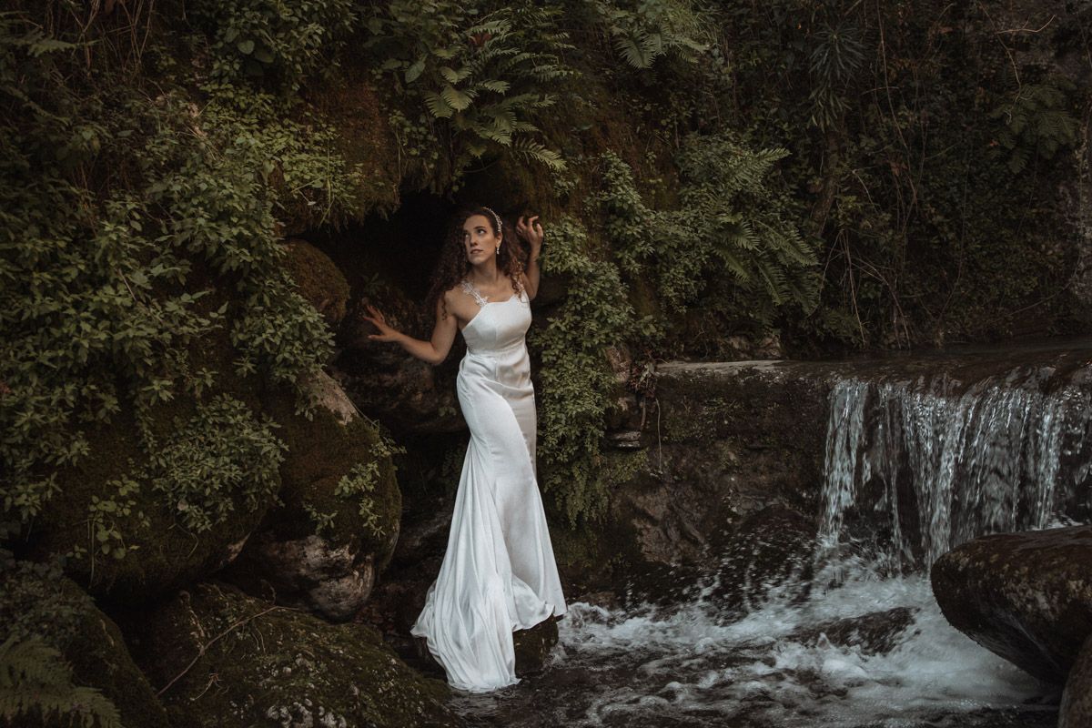 A white wedding dress creates contrast against a natural waterfall setting.