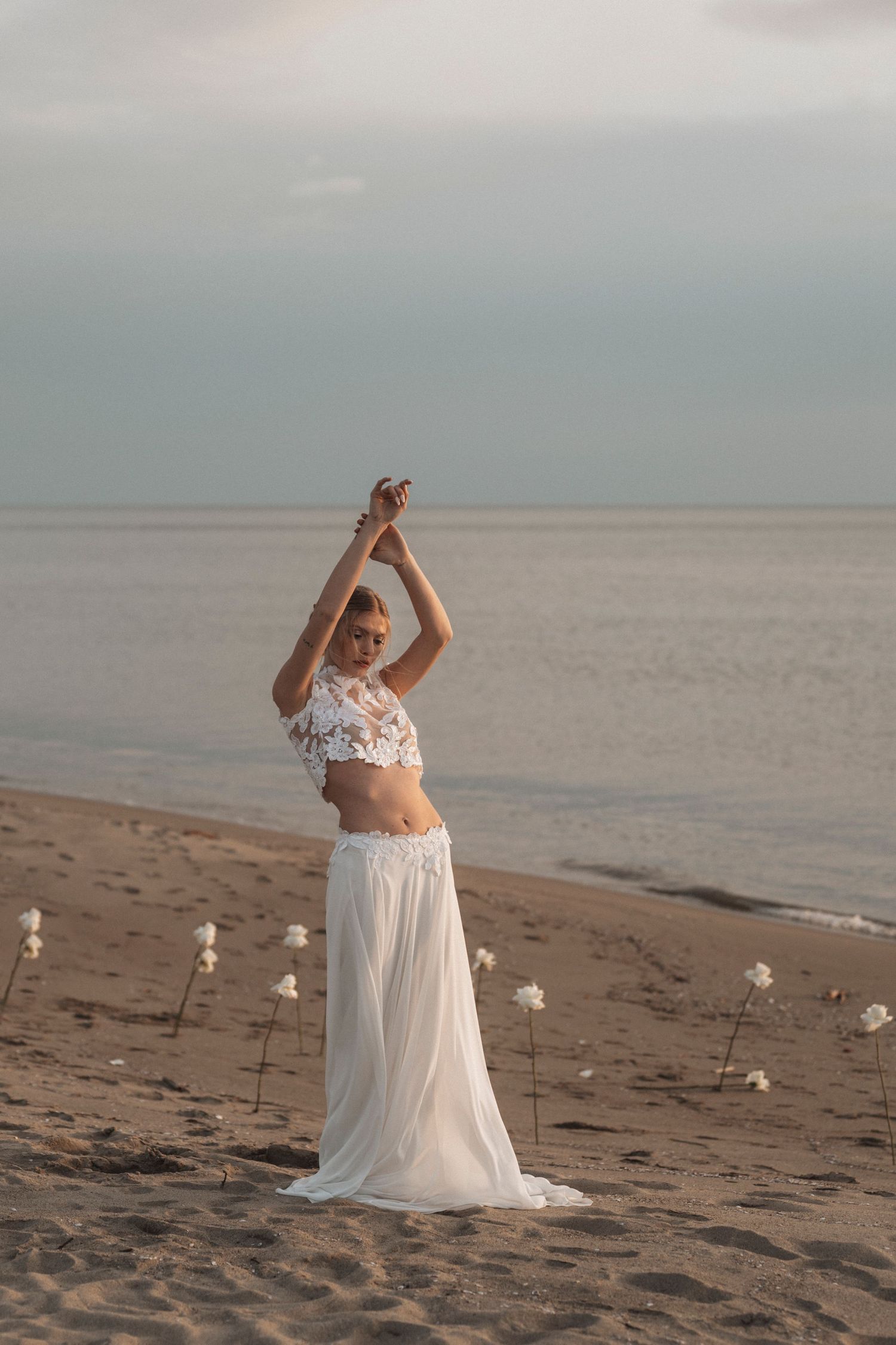 A white flowy dress ensemble on a beach with candles at sunset creates a romantic atmosphere.