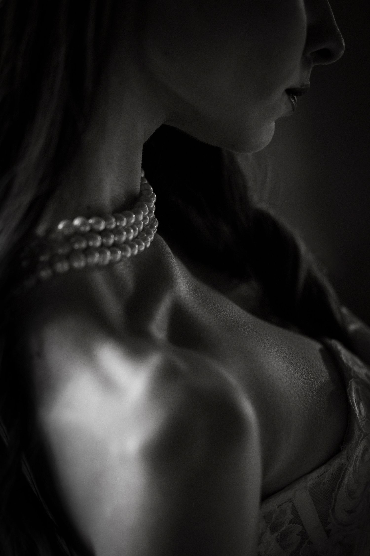 Artistic black and white portrait showing a pearl necklace against a dark background.