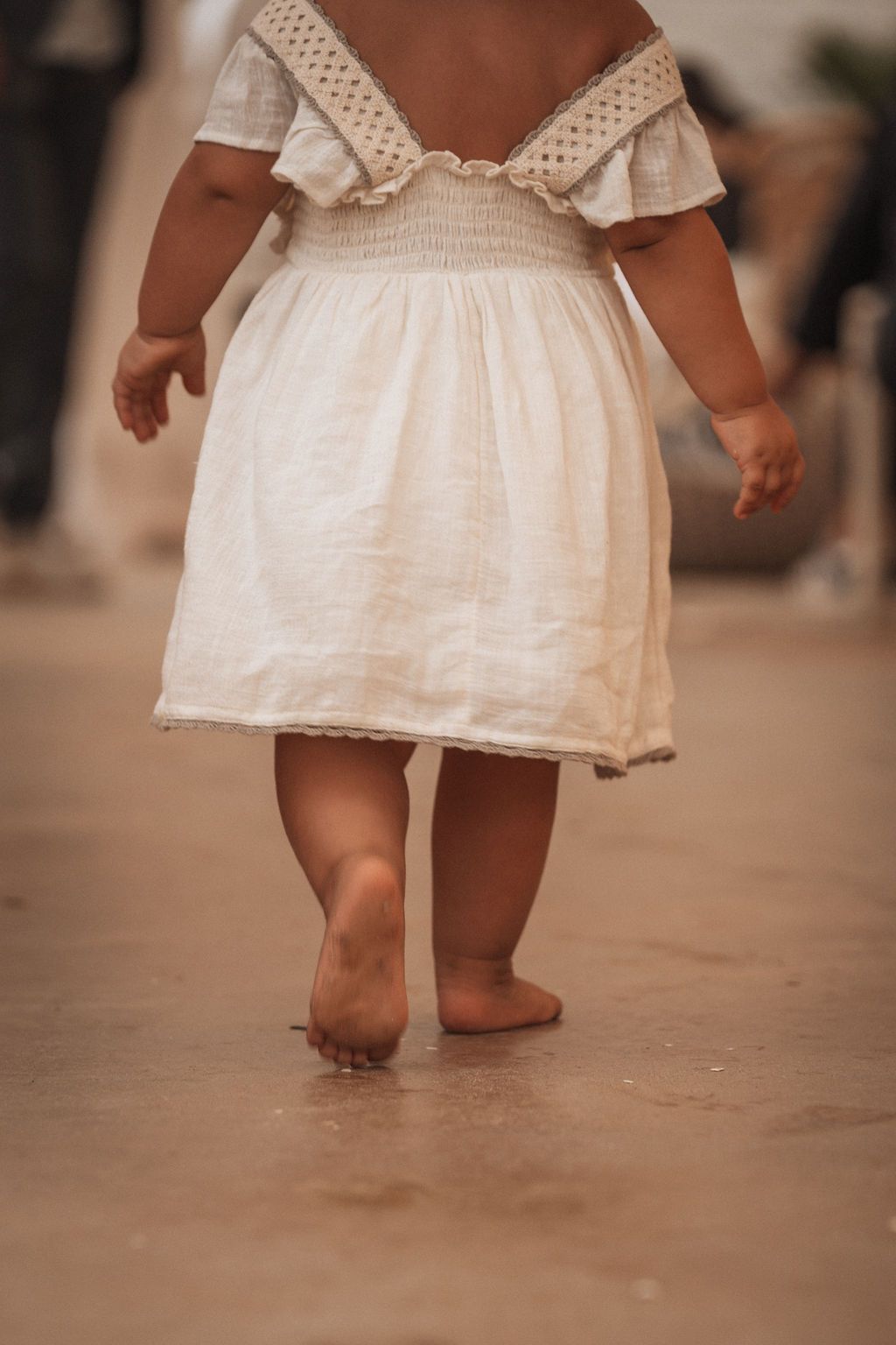 Small feet in a white lace dress walking on a rustic floor.