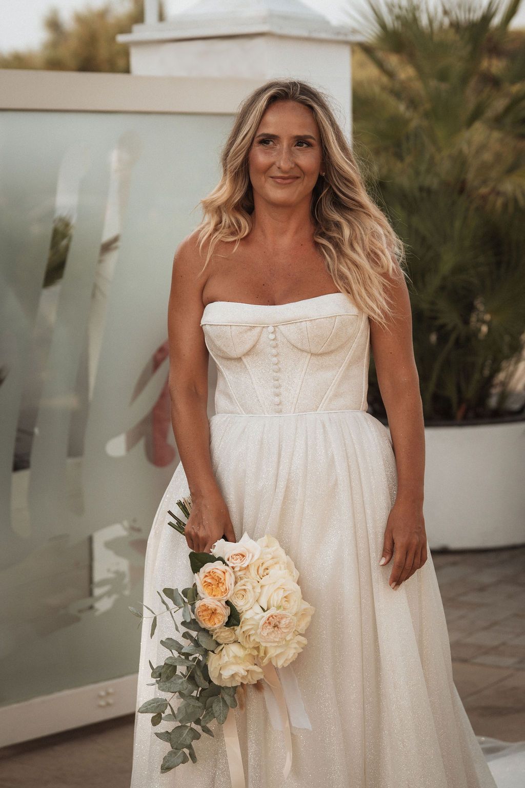 Wedding party members in flowing white dresses holding romantic peach and cream bouquets.