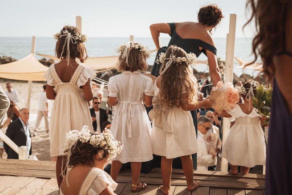 Wedding ceremony guests gathered on a sunny beach with white and cream colored attire.