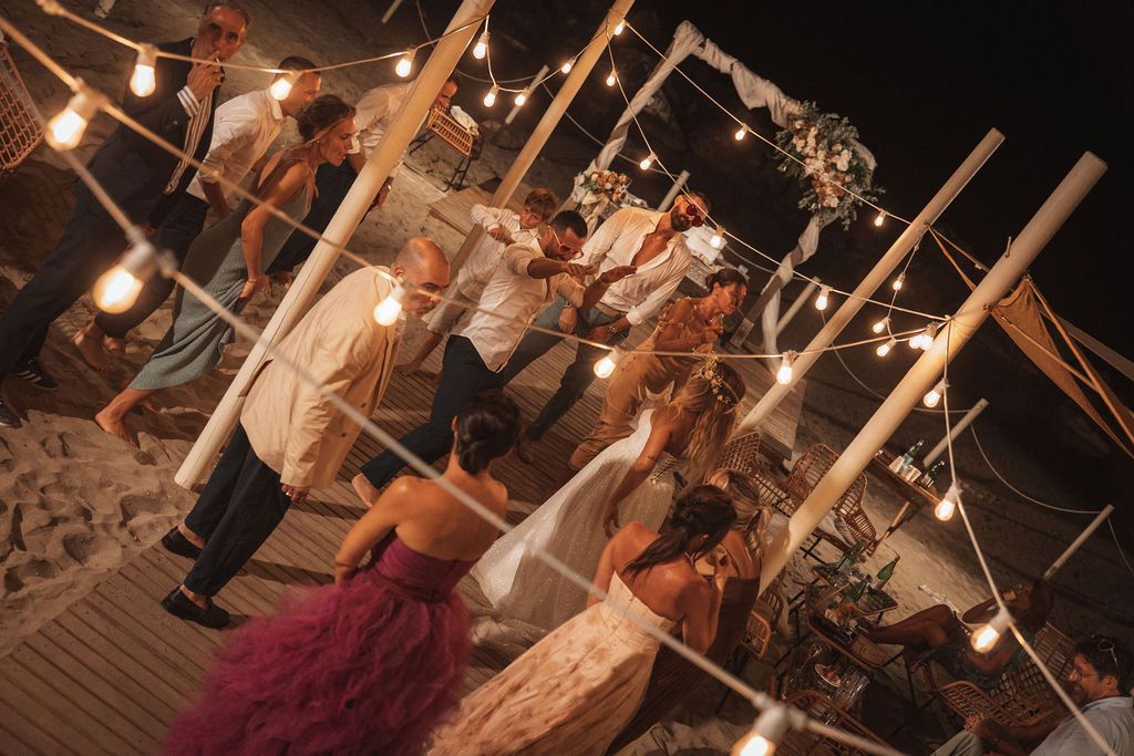 Wedding party celebrates on a decorated outdoor deck with string lights and wooden posts at night.