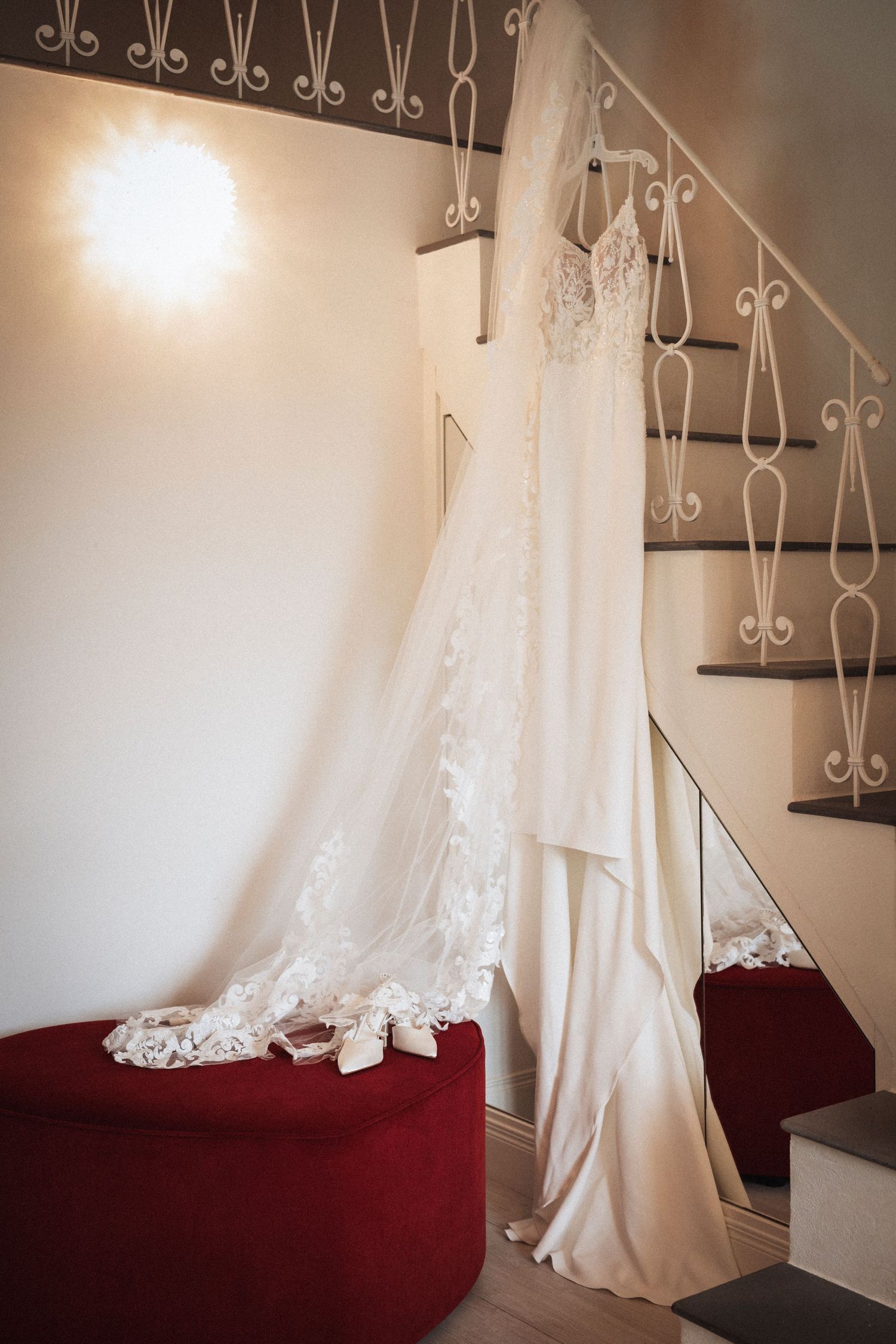 White wedding dress hanging on decorative metal rack against neutral wall with elegant lace details.