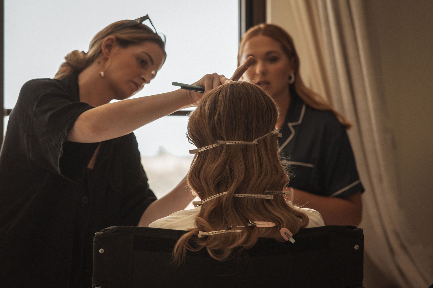 Professional stylist working on wedding day hair preparation in natural light.