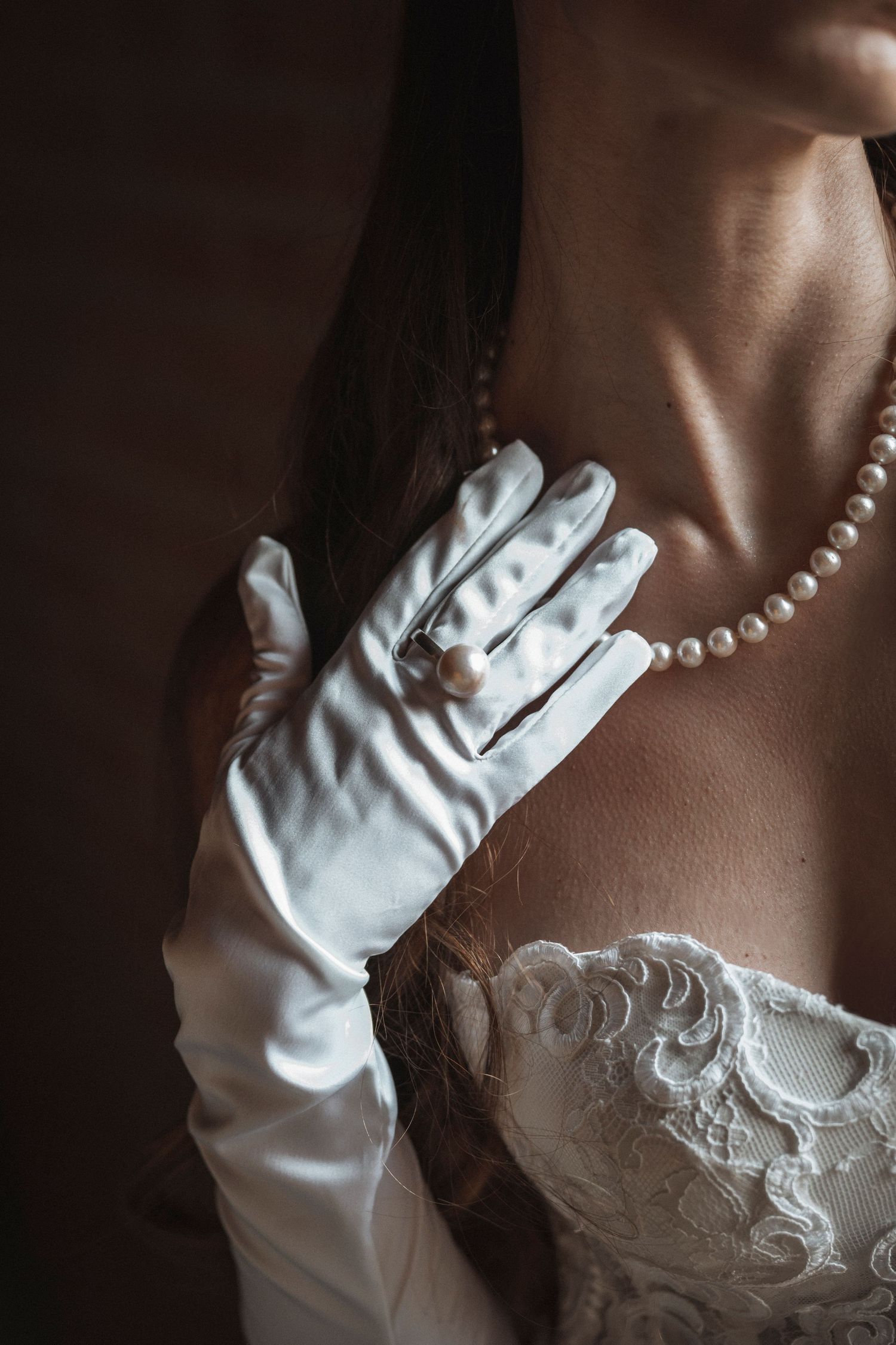 A person wearing white gloves and pearl necklace poses with hands gracefully positioned.