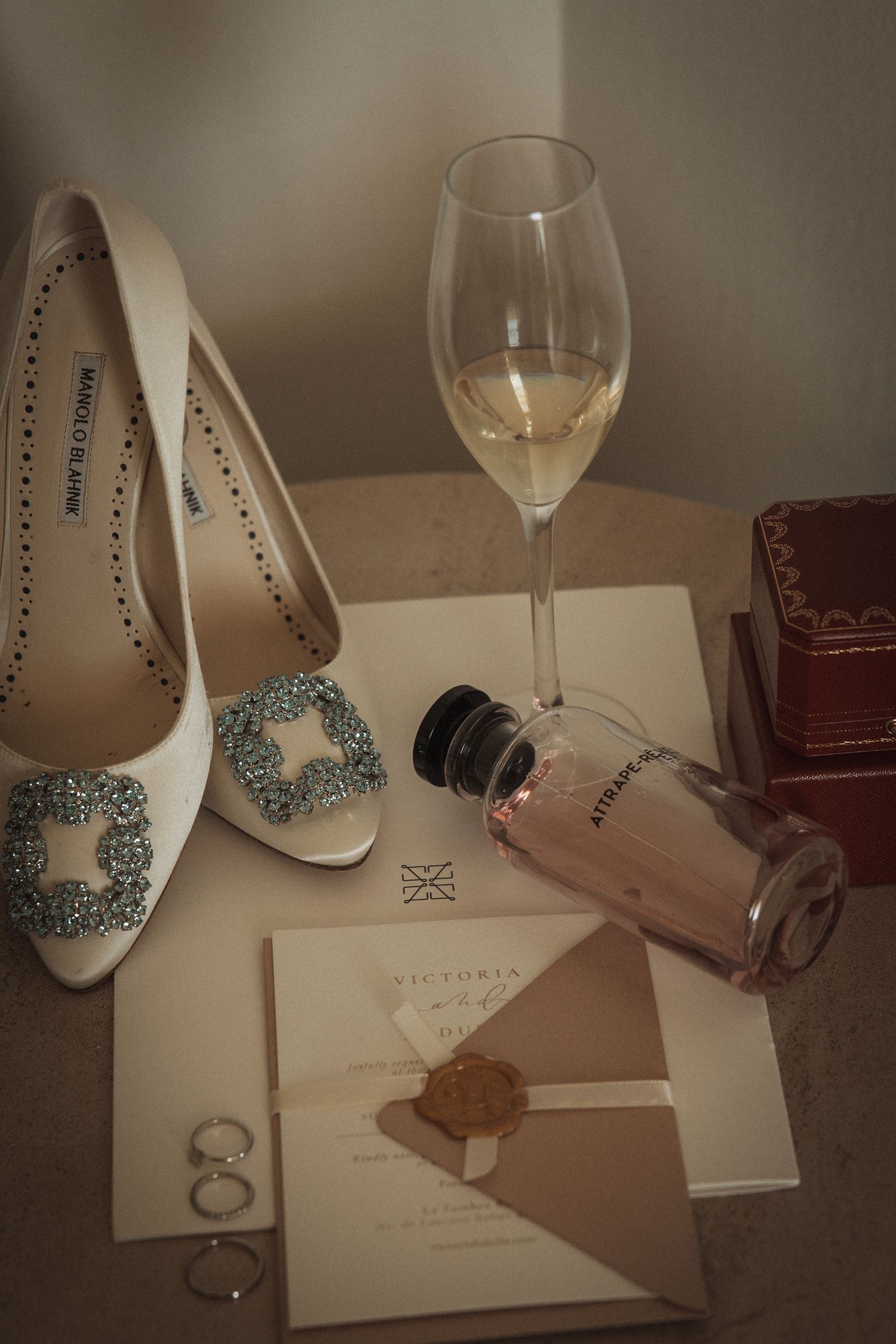 Wedding accessories including white heels, wine glasses, and invitation cards arranged on a table.