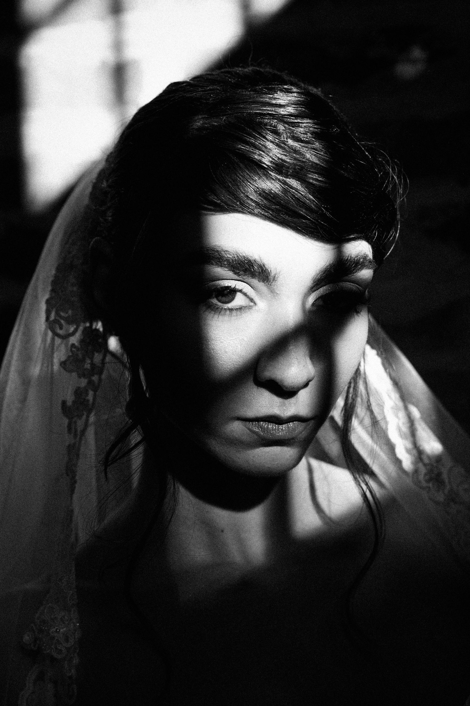 Dramatic black and white portrait with strong shadows and a delicate veil creating a moody artistic composition.