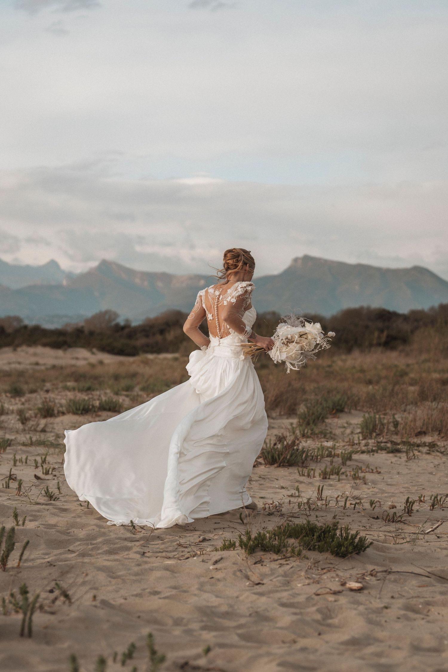 Flowing white wedding dress billowing dramatically against a desert mountain landscape.