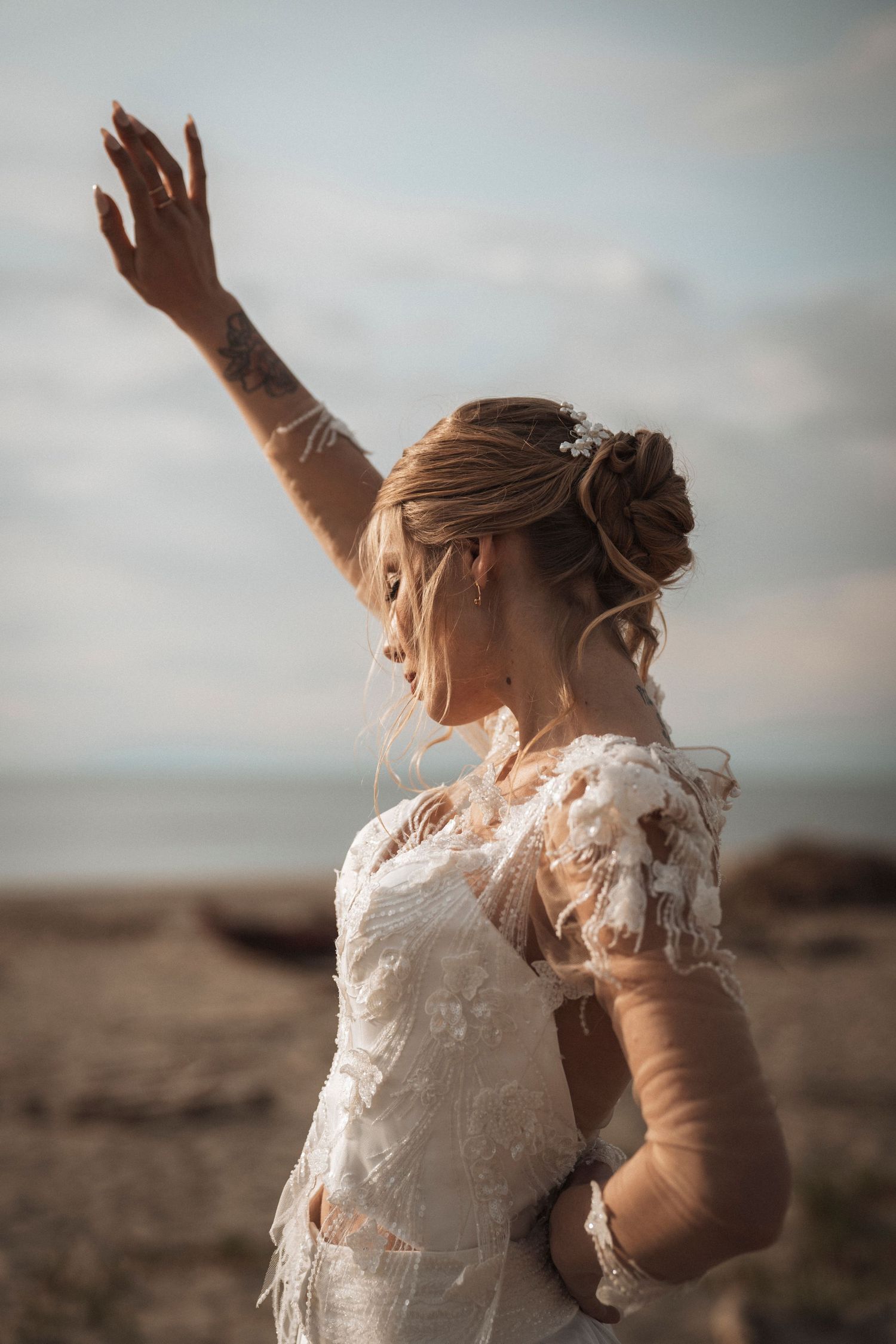 Artistic bridal portrait with outstretched arm wearing delicate lace wedding gown against desert landscape.