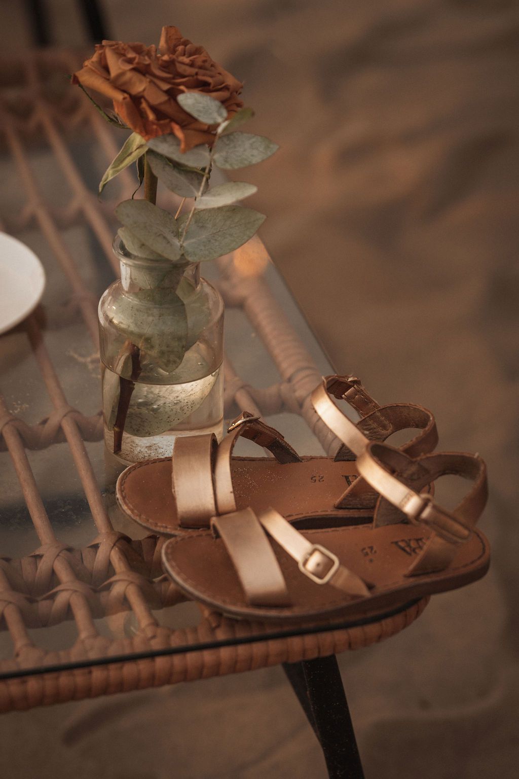 Rose gold sandals with floral decorations displayed on wooden slats.