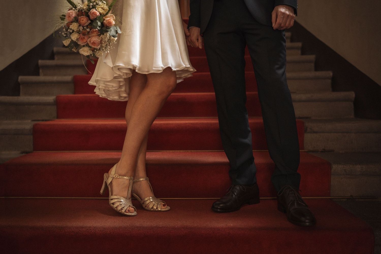 Couple's feet on elegant red carpeted stairs during a wedding celebration.
