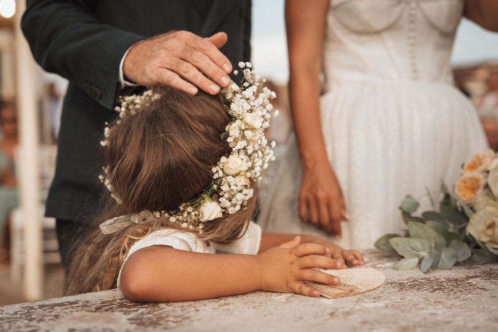 Wedding ceremony details with floral headpiece and white dress on wooden deck.