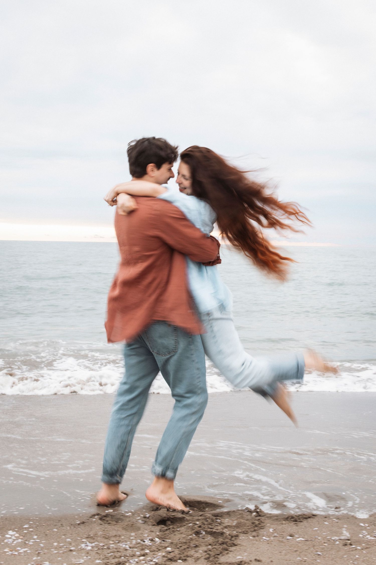 Playful couple spinning and dancing together on a beach at sunset.