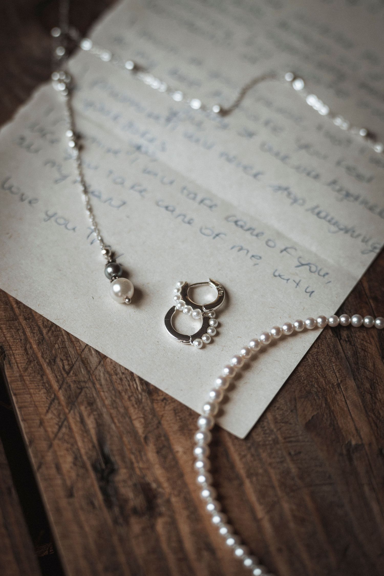 Pearl necklace and silver earrings arranged on handwritten wedding vows.