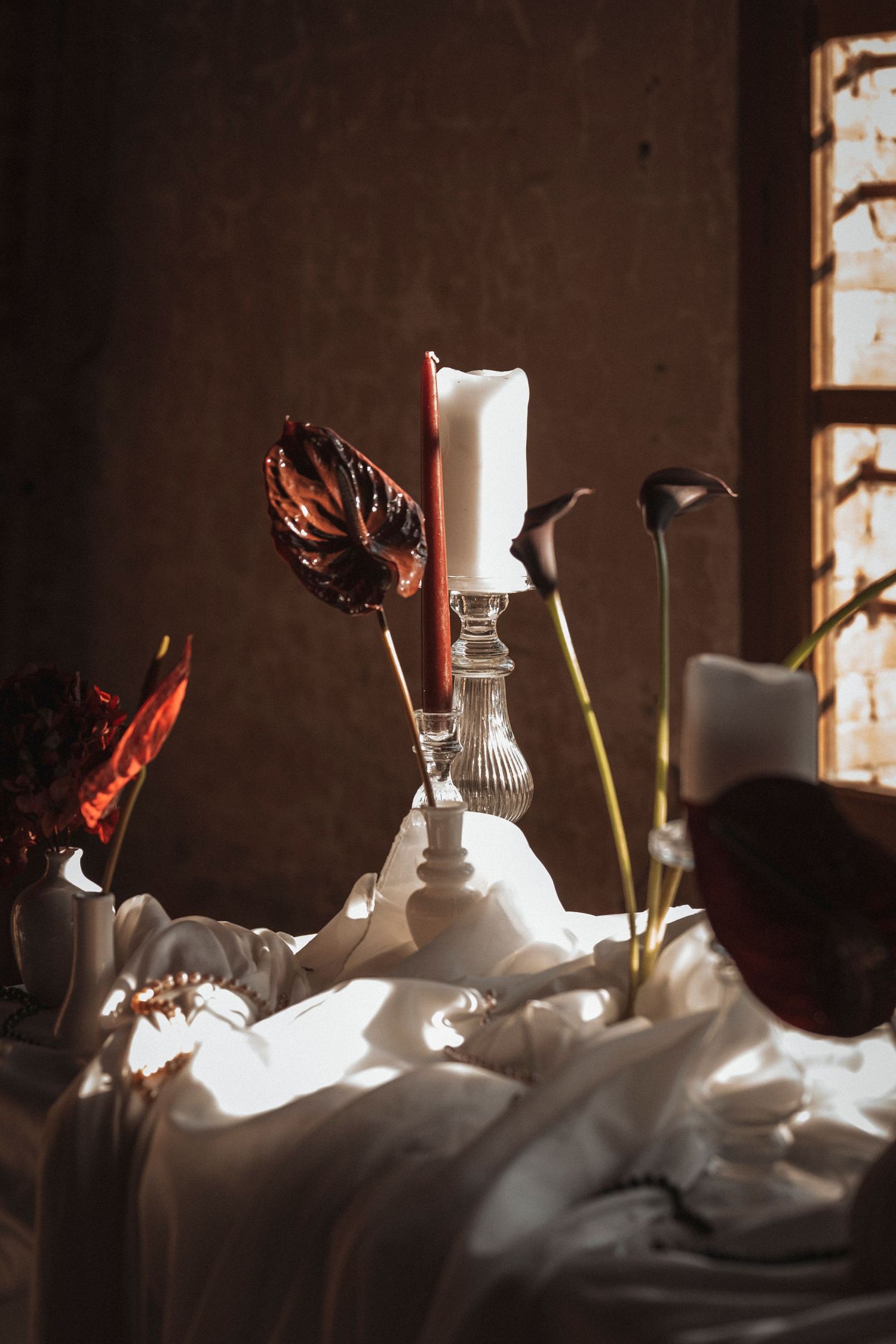Artistic still life composition of white vases and glassware with dramatic shadows against a dark background.