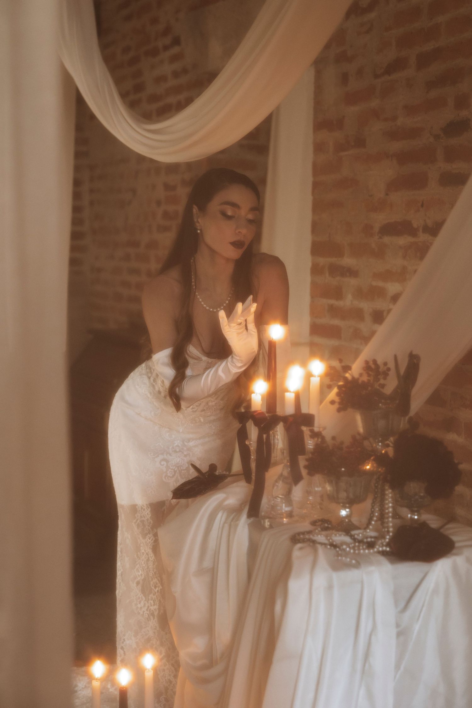 Candlelit scene with white drapes and elegant table settings in brick-walled room.