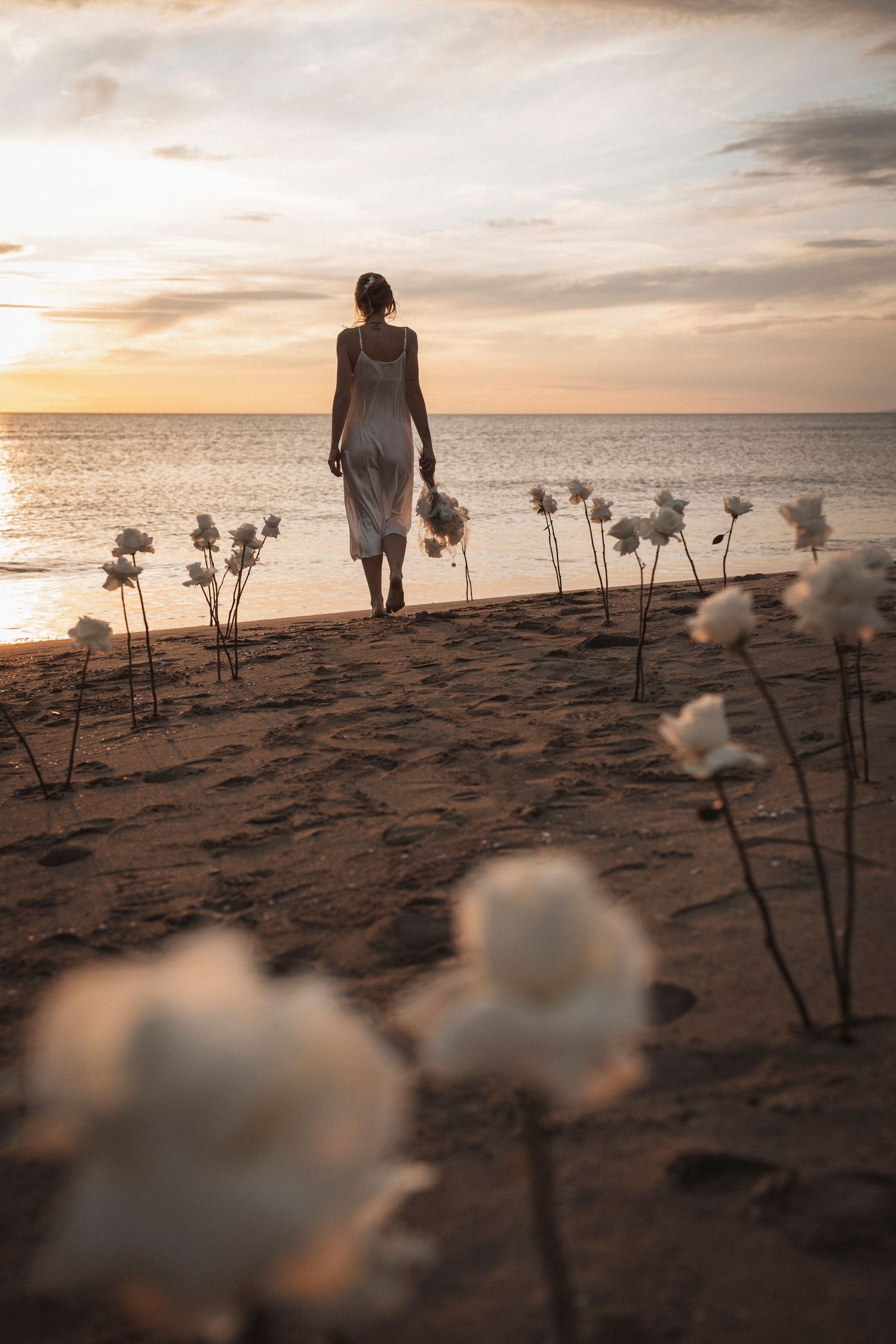 Silhouette with white cotton flowers on beach during golden hour sunset.