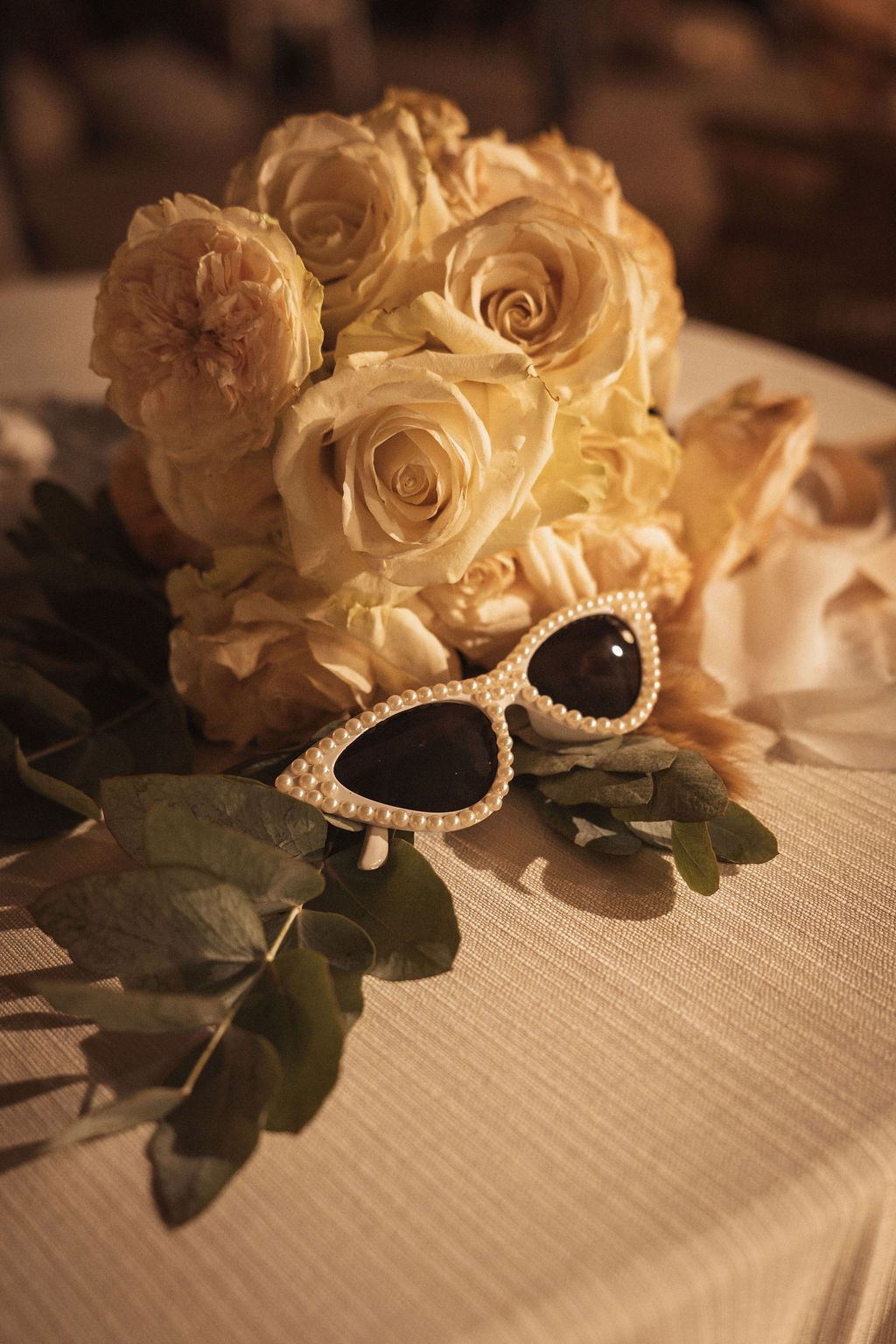 Elegant white roses and pearl-adorned sunglasses arranged on textured fabric.