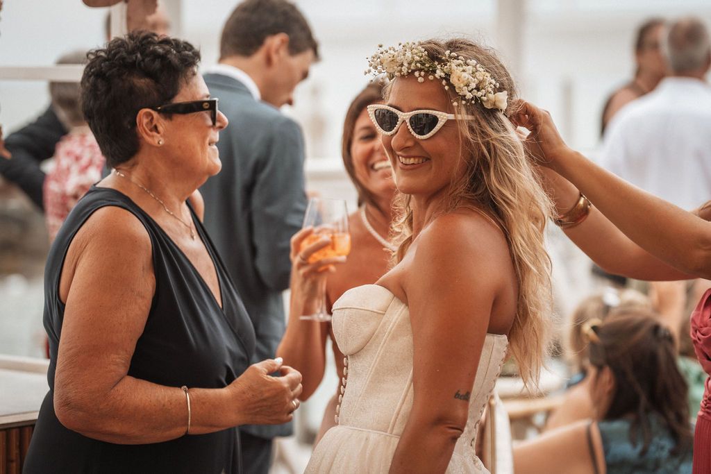 A bride in a white dress and retro sunglasses celebrates with guests at a wedding reception.