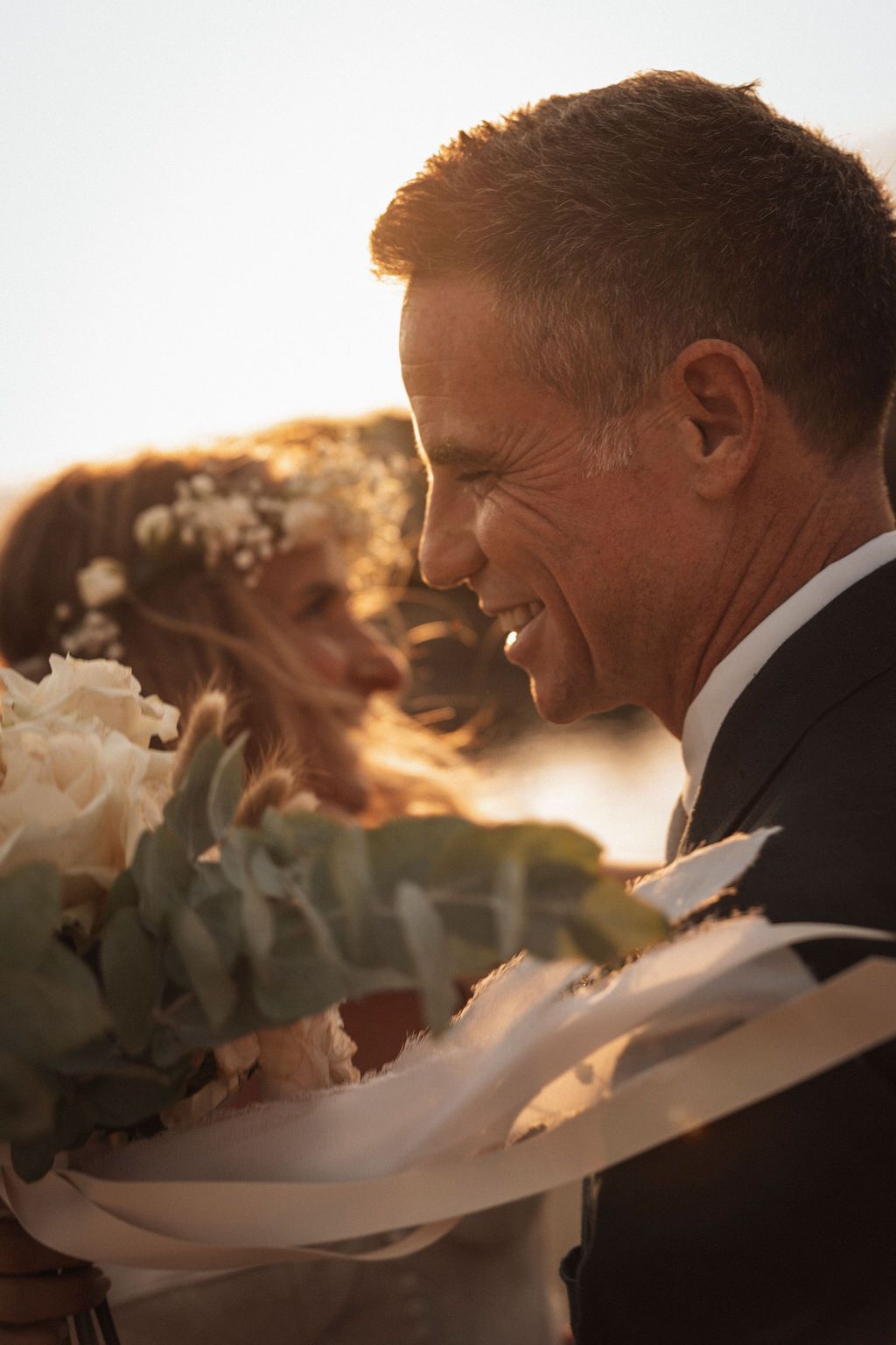 Golden sunset silhouettes of a couple with white flowers and flowing ribbons.