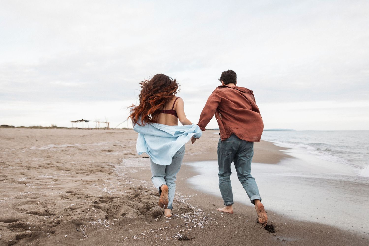 Playful couple running along a sandy beach at sunset.