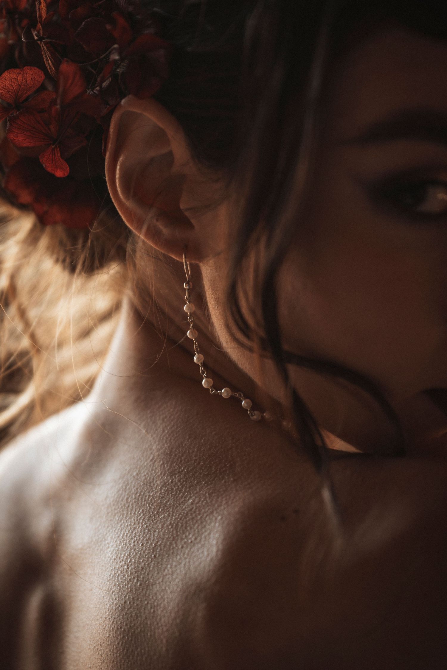 Close-up detail of delicate bridal jewelry and lace against soft natural lighting.