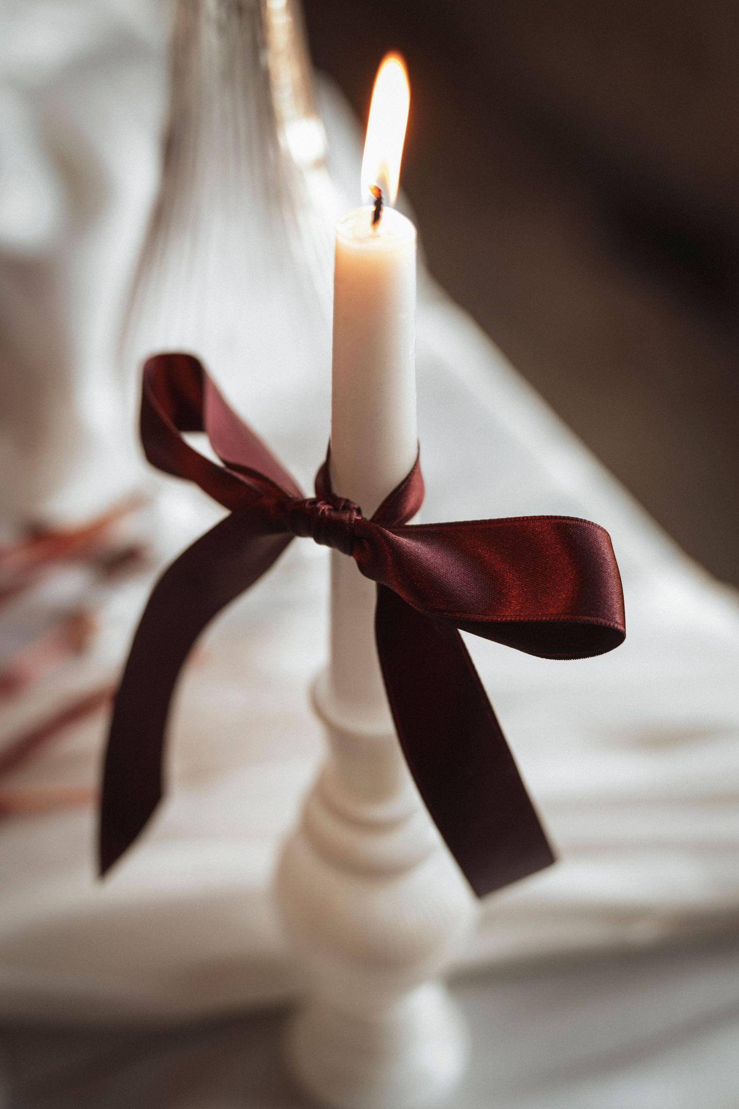 White candles decorated with burgundy ribbons create an elegant display in soft focus.