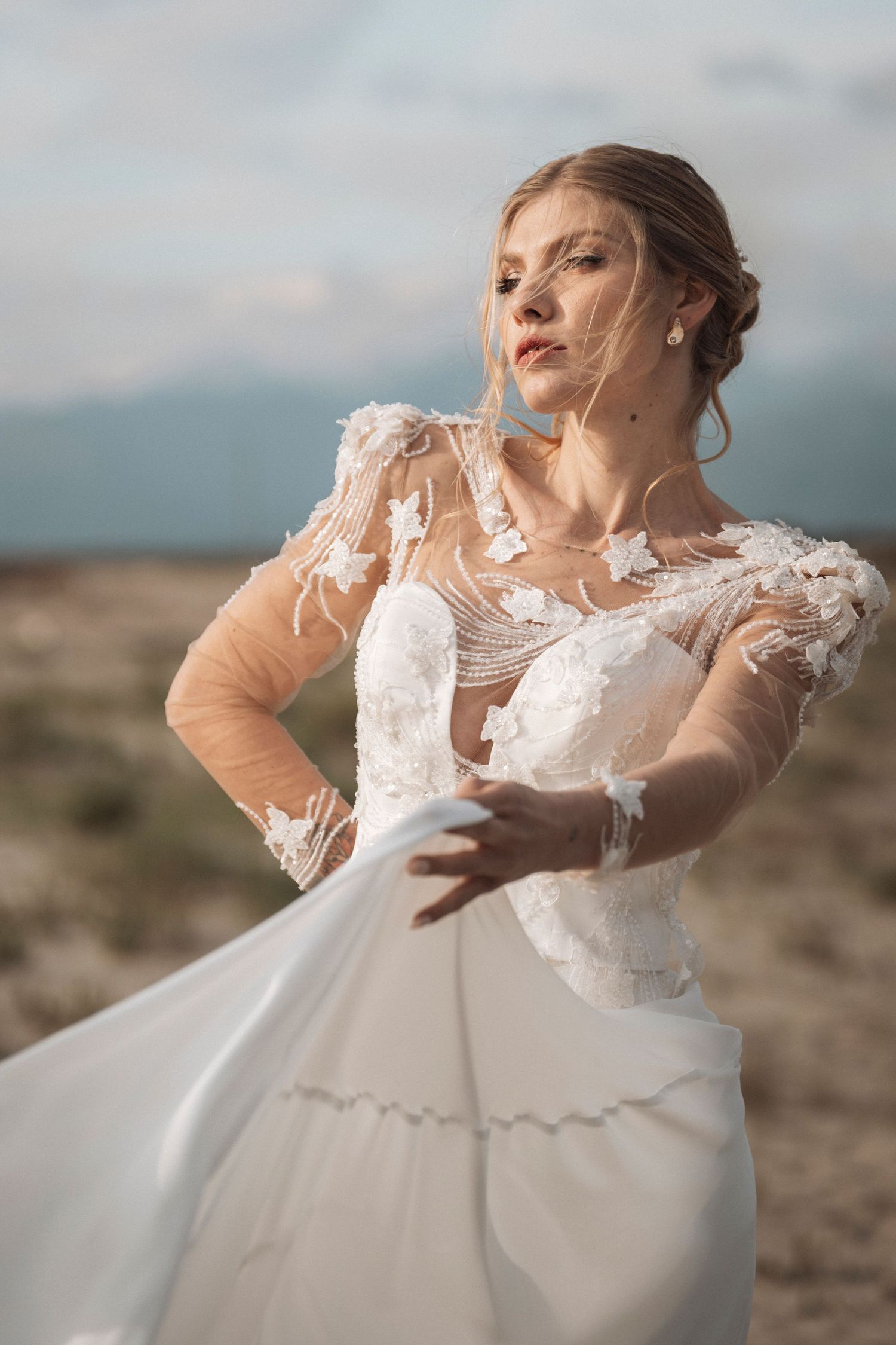 A wedding dress with delicate lace sleeves and flowing skirt photographed against a mountainous desert landscape.