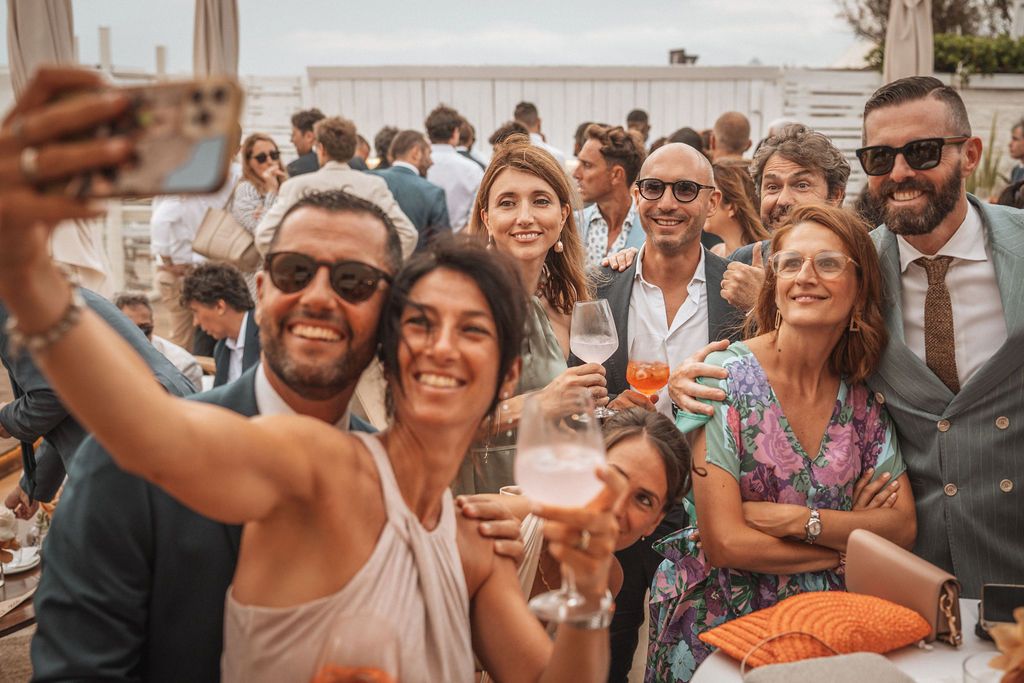 Wedding guests take a group selfie while celebrating at an outdoor reception.