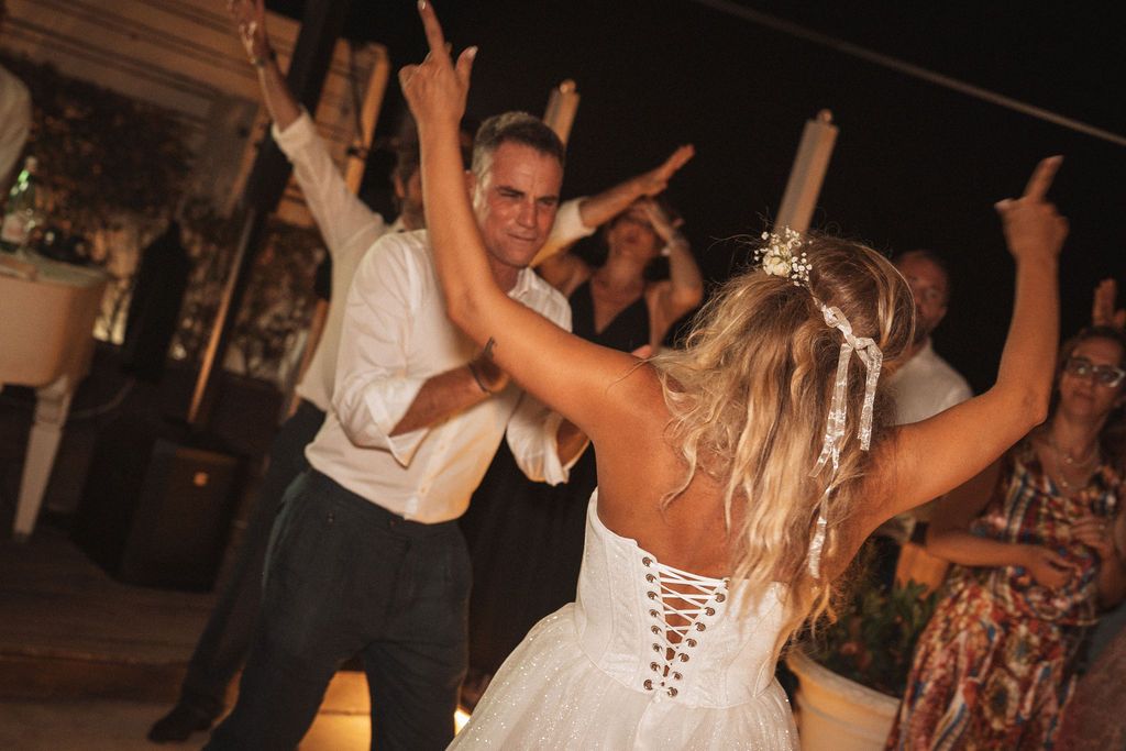 Wedding guests dance energetically on a dance floor with string lights overhead during an evening reception celebration.