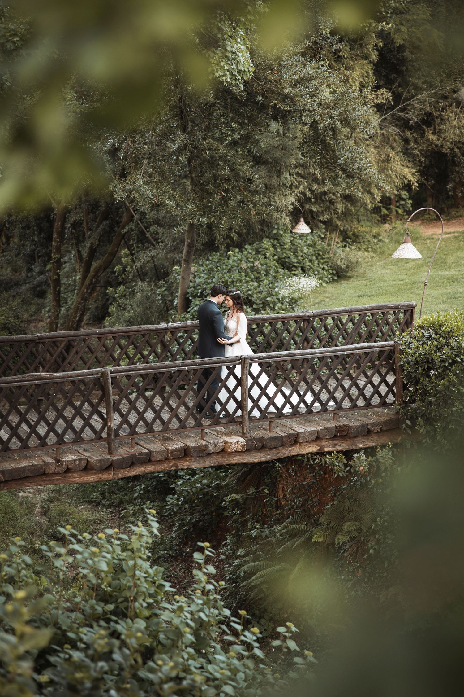 Couple walking across rustic wooden bridge surrounded by lush greenery.