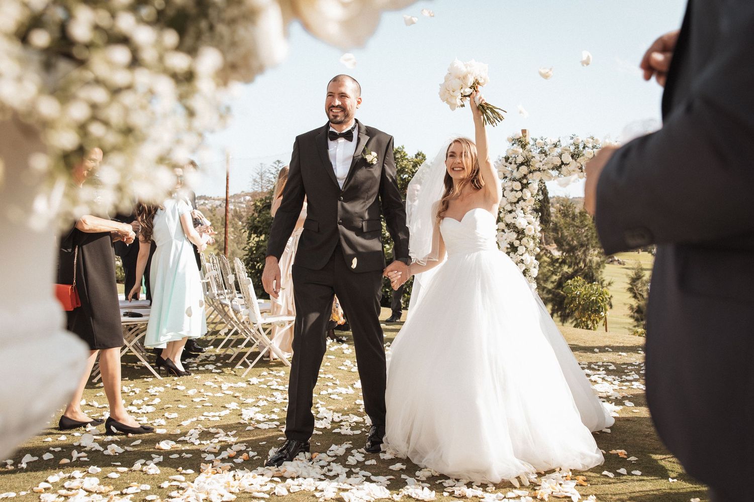 Wedding party members walk and laugh together on a sunny outdoor path.