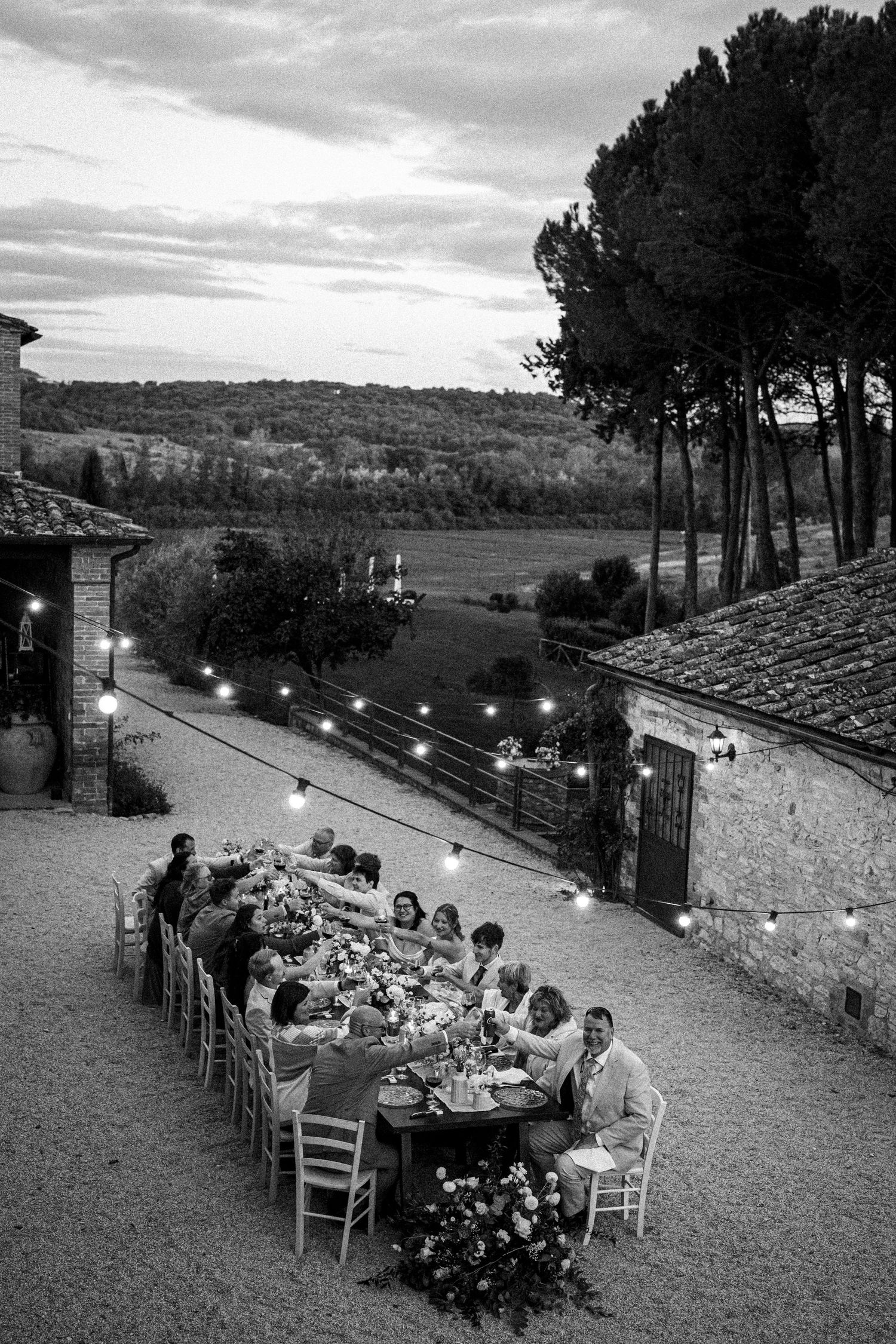 Black and white aerial view of outdoor wedding dinner with string lights and scenic countryside.