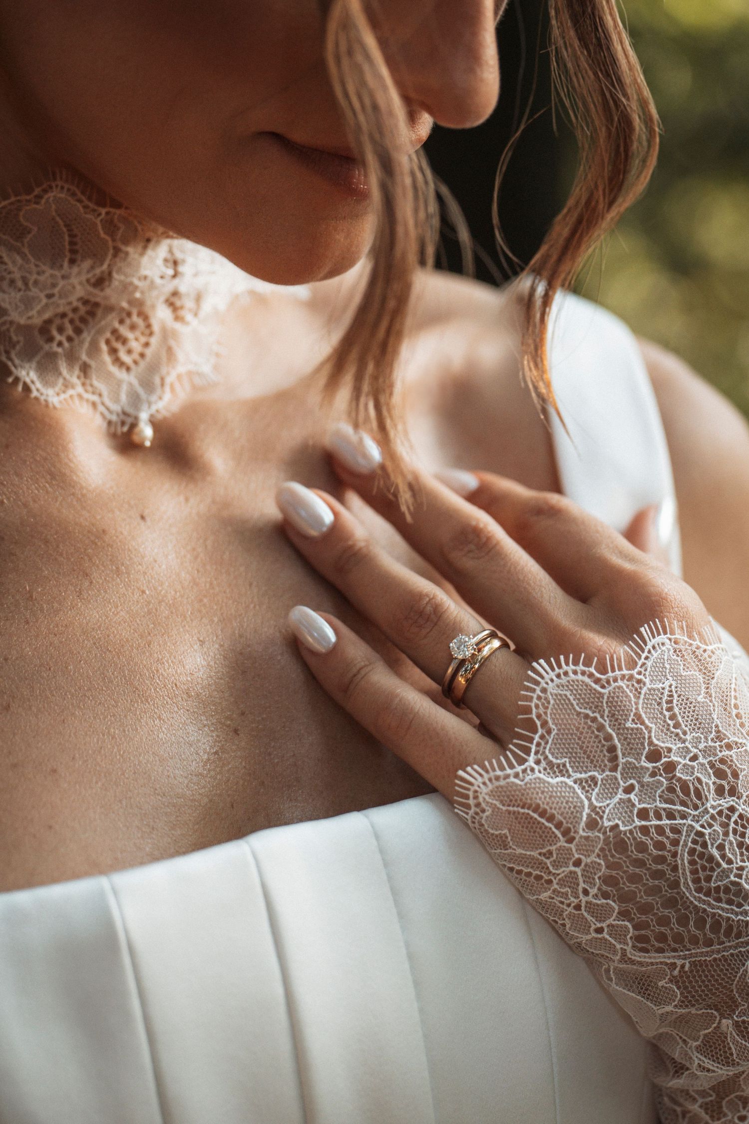 Close-up of bride in lace wedding dress showcasing elegant gold engagement ring and manicured nails.