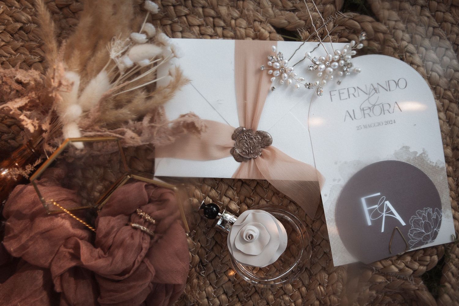 Wedding details including rings, invitations, and floral decorations arranged on textured stone surface in warm lighting.