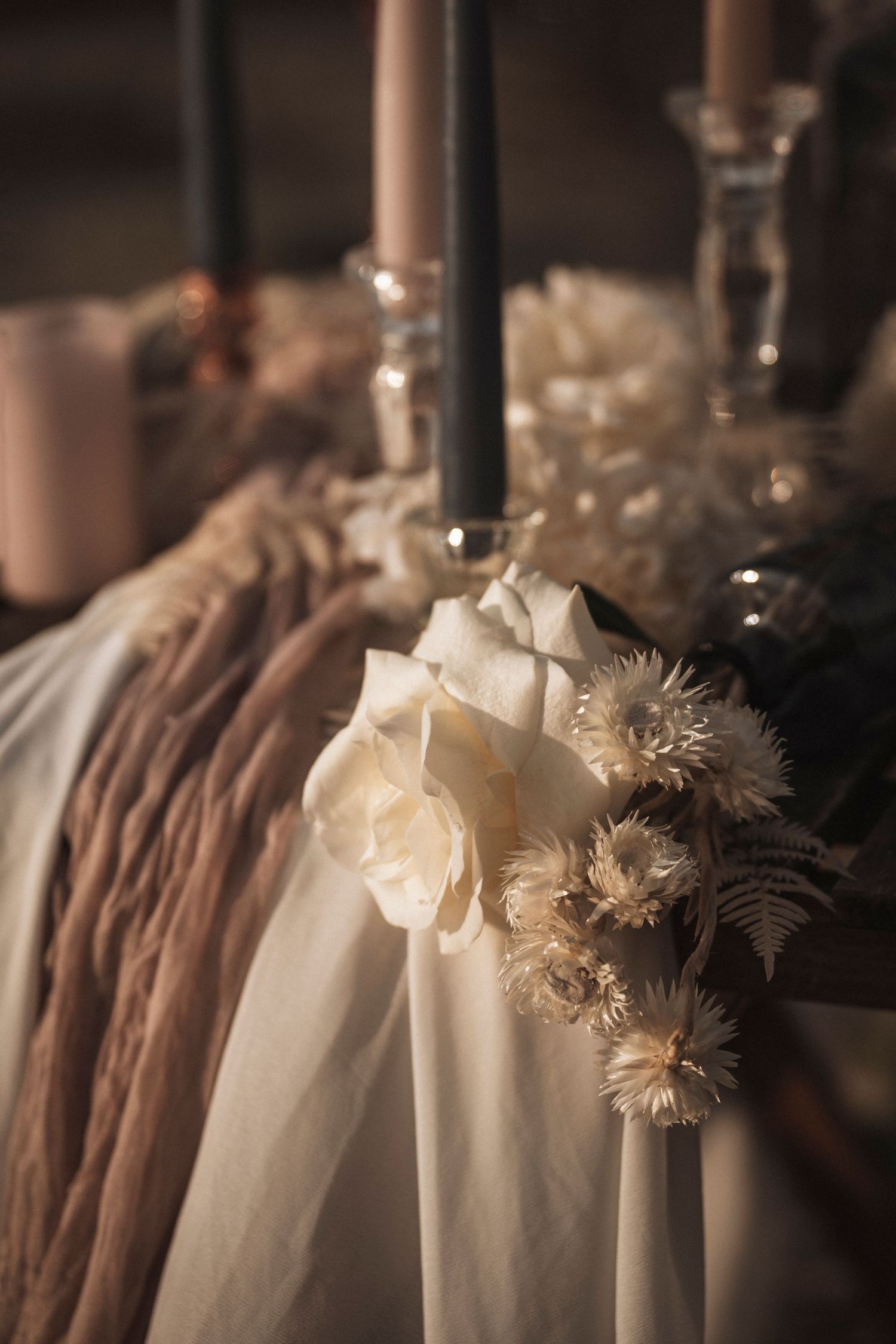 Elegant white roses and dried flowers arranged with black candles and delicate fabric in a romantic vintage setting.
