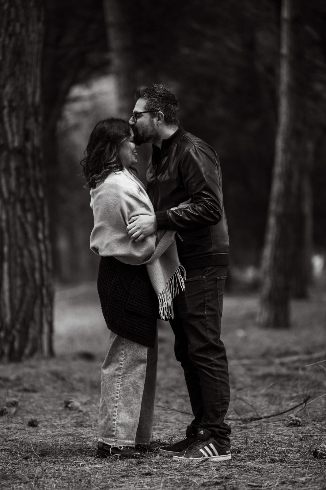 A romantic black and white photo of a couple sharing an intimate moment in a wooded forest setting.