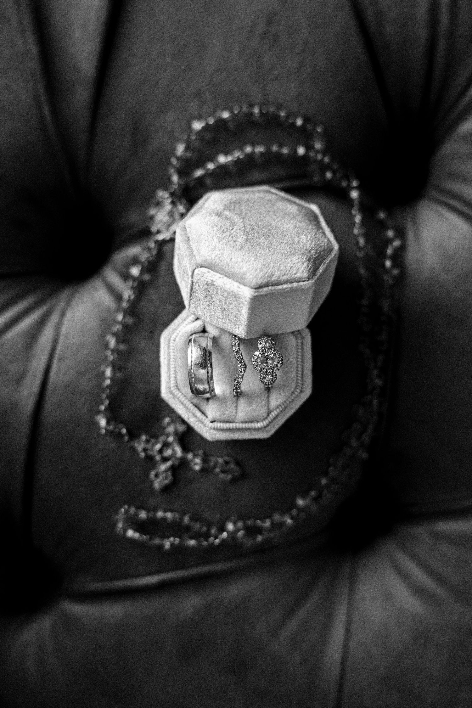 Black and white close-up of an ornate ring box with jewelry on dark velvet background.
