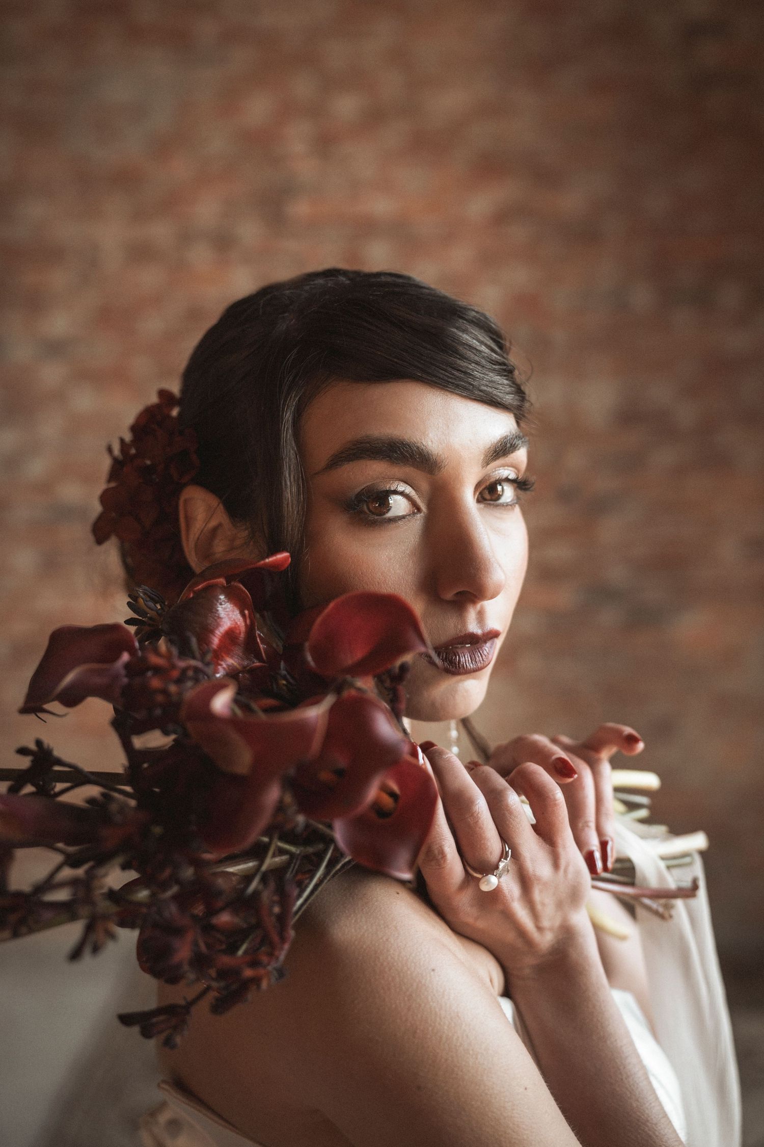 Artistic portrait with deep red floral elements against exposed brick backdrop.