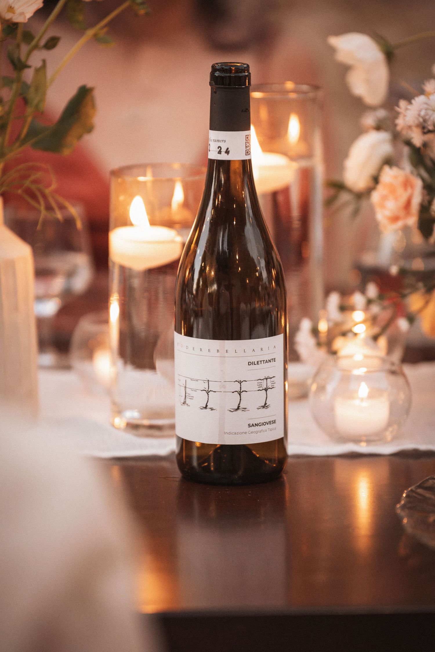 Wine bottle and glowing candles create romantic ambiance at wedding reception table.