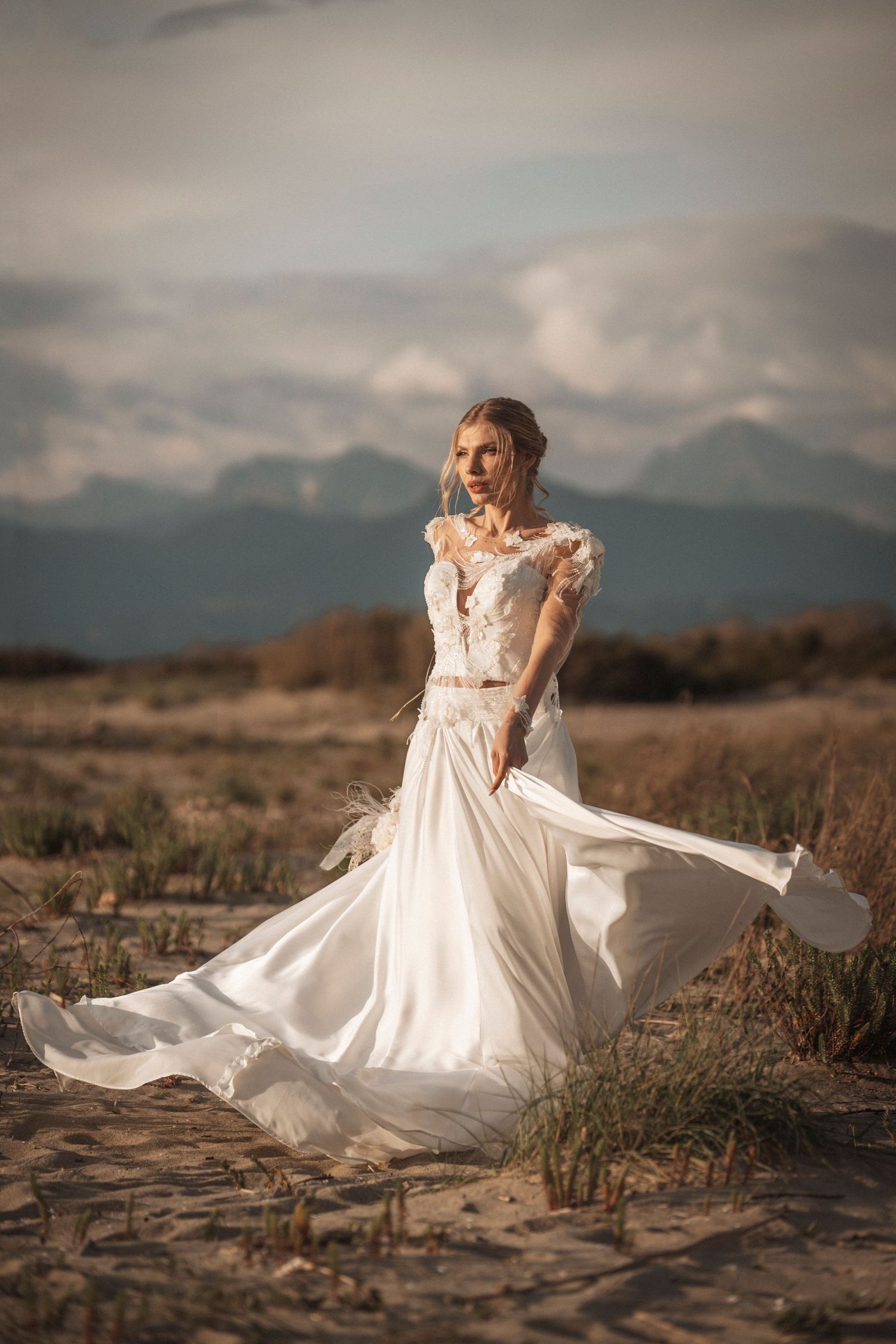 An ethereal white wedding gown flows in the wind against a mountainous desert landscape.