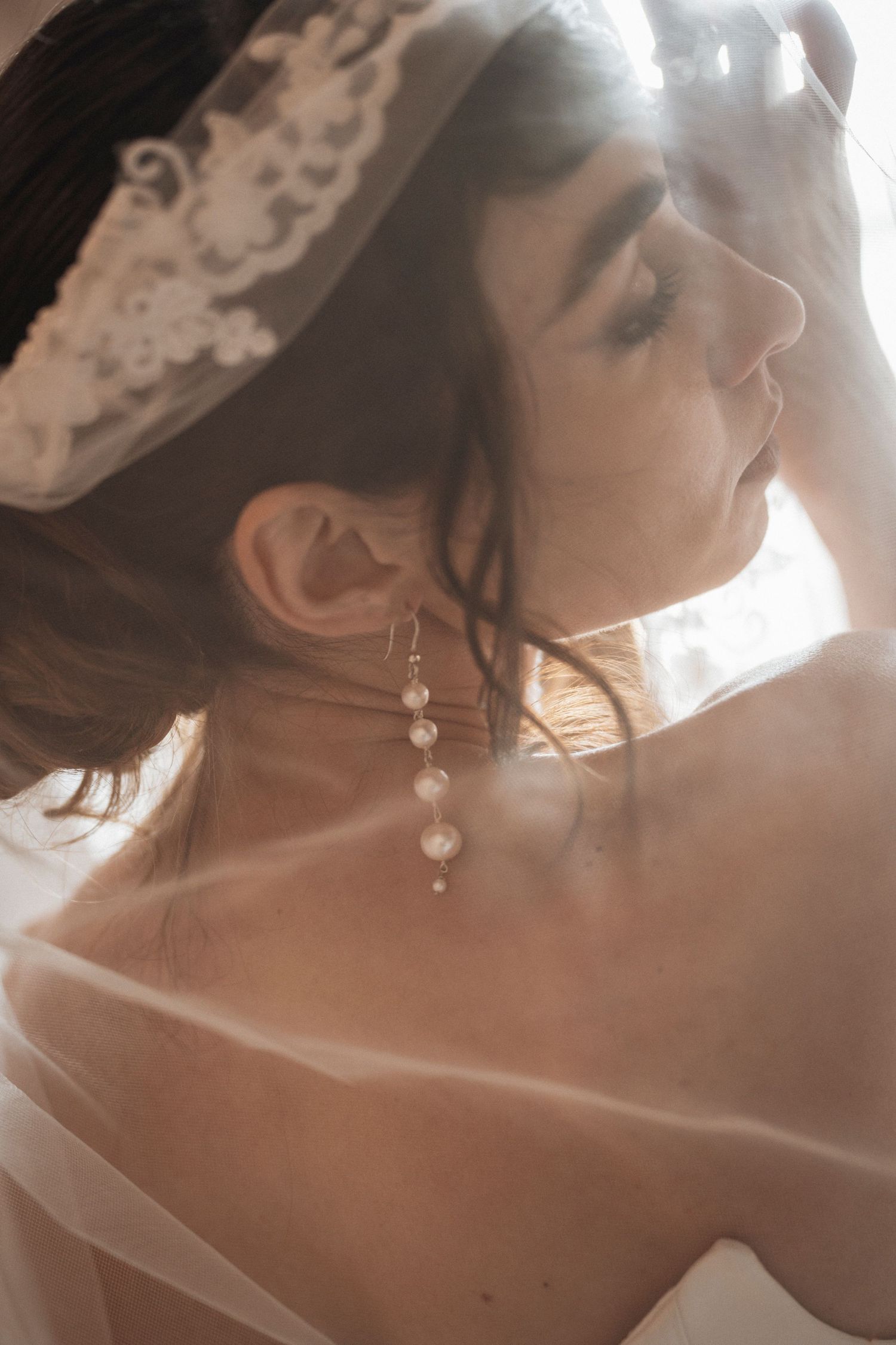 Soft dreamy portrait with pearl jewelry and delicate veil in warm sunlit tones.