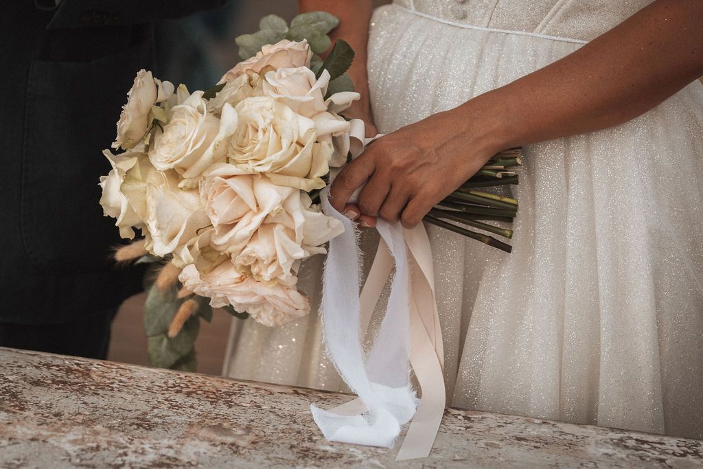 Hands holding elegant white and peach floral bouquets against white formal attire.