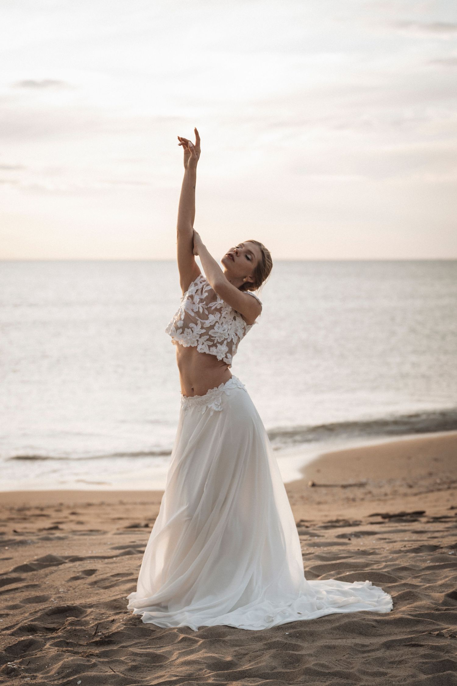 Modern two-piece wedding dress with lace crop top and flowing skirt captured during sunset on a beach.