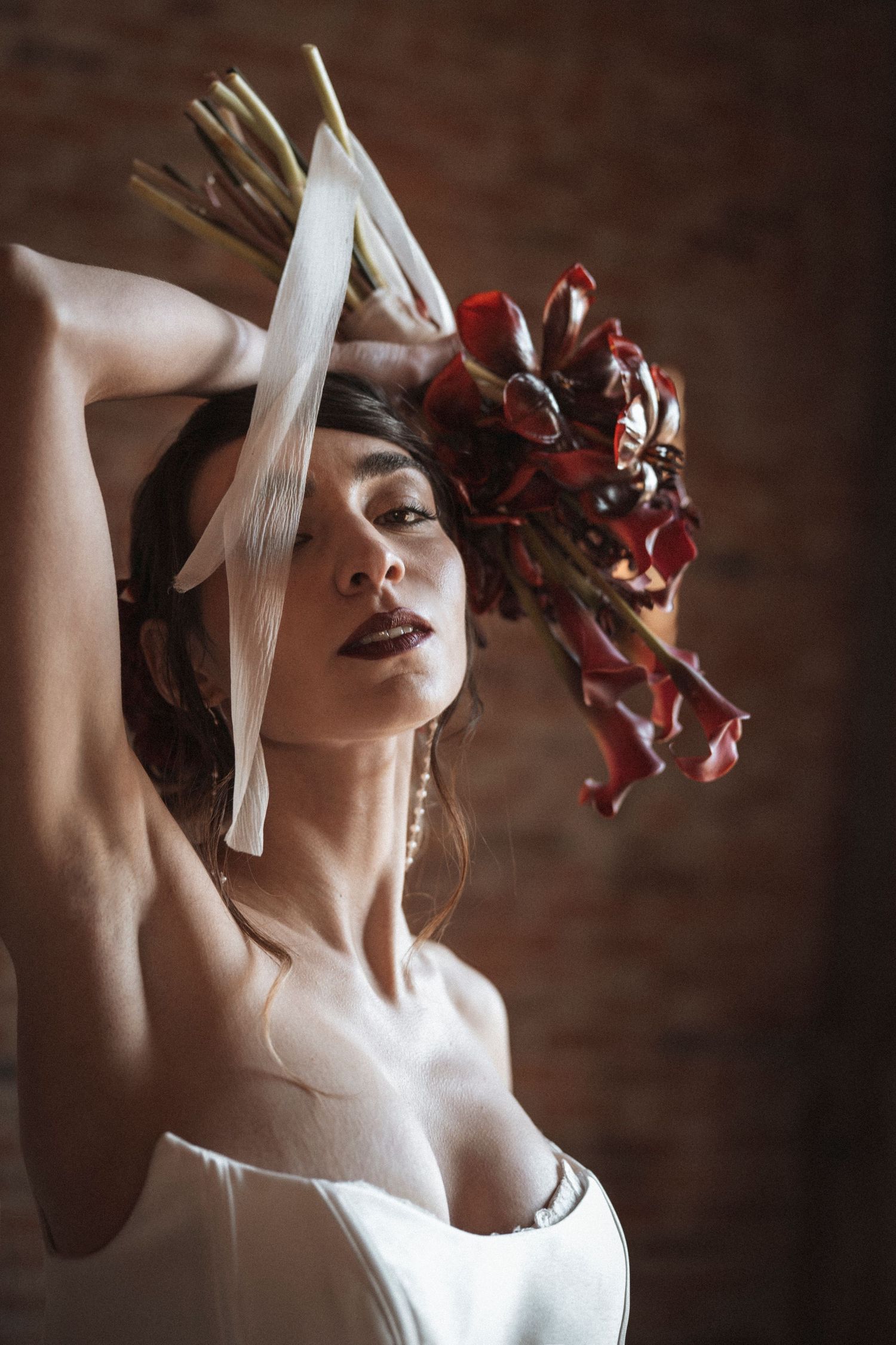 Dramatic bridal portrait with red floral headpiece against brick wall.